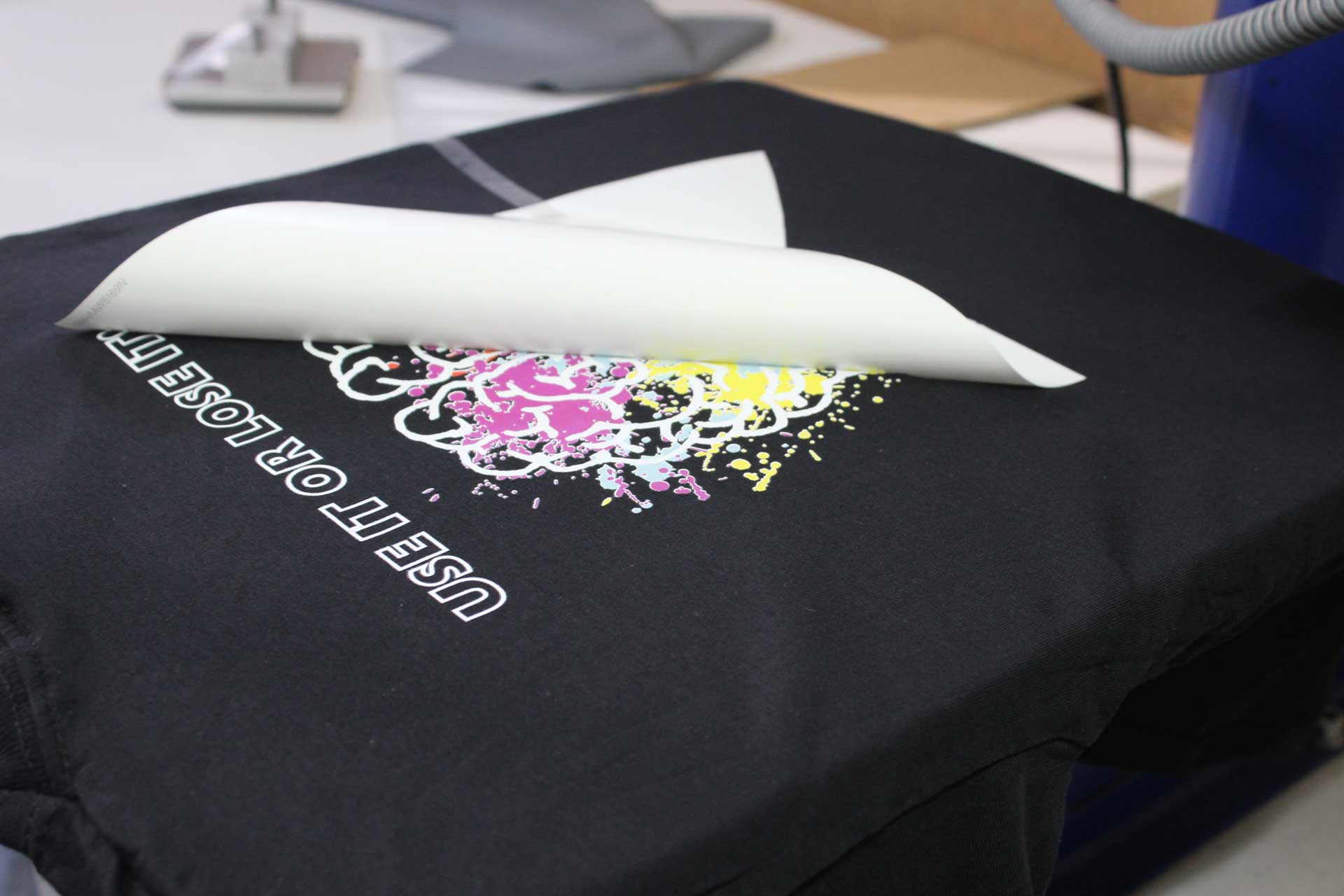 Schwarzes T-Shirt beim Textildruck mit abgezogener Transferfolie und farbigem Printmotiv
